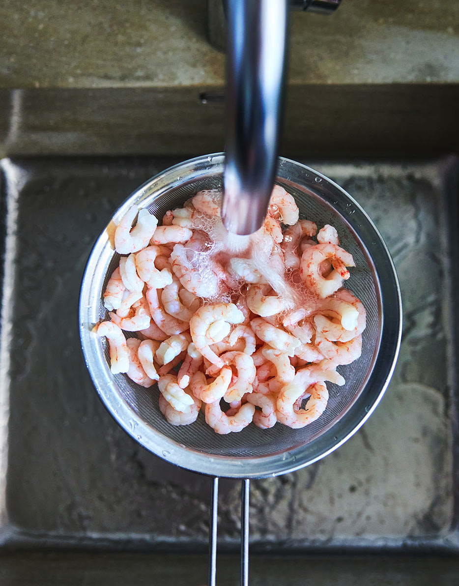 Defrosting prawns by running cold water through them in a sink